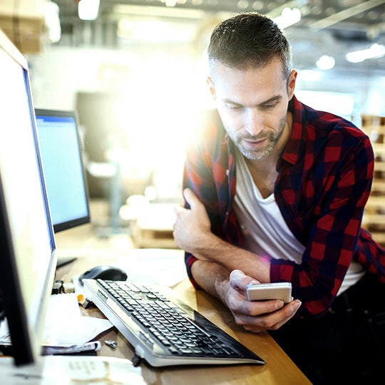 man at his computer looking at a smartphone